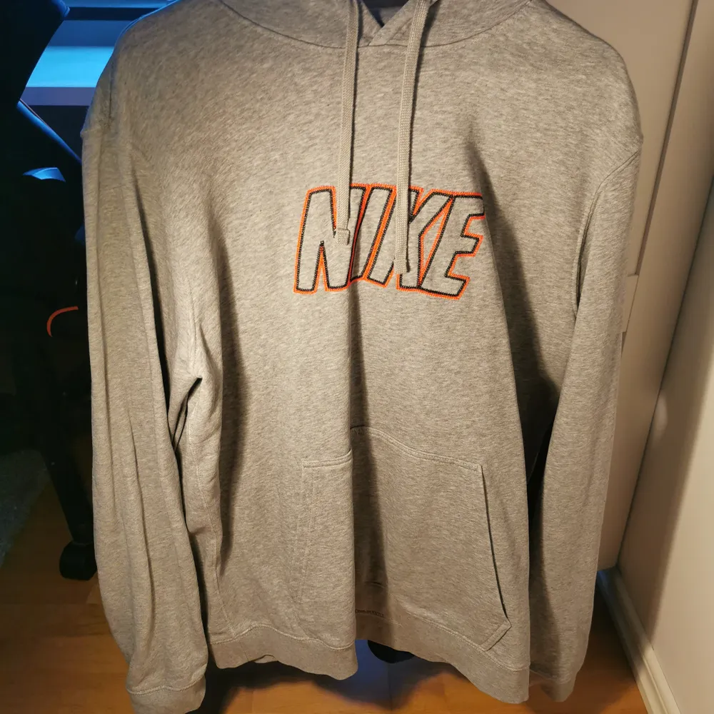 Säljer en hoodie från Nike i grå med loggan broderad i orange då jag inte använder längre. Tröjan är i XL och är i fantastiskt skick också. . Hoodies.