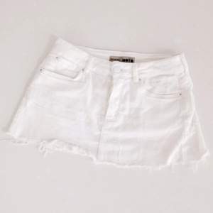 Kortkort vit kjol från Topshop med slitna kanter. Knäppning med 4 knappar. Storlek S, W26. 
97 % bomull, 3 % elastan.