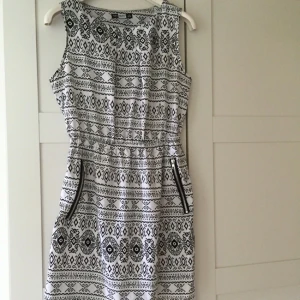  - Svart och vit mönstrad klänning i lite syntetiskt material, med blixtlåsfickor  