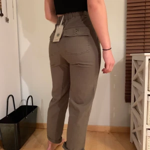 Pull & Bear - Kakibyxor strl. XS - Kakifärgade byxor med knytning i midjan. Helt nya och säljes för att de tyvärr är för små 😢 (min syster på bilden) Nytt pris är 352kr men säljer för 150kr. Ser mer gröna ut i verkligheten, som på bilden från ASOS där de är beställda. 