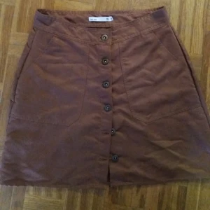  - Kjol med knäppning i mocka-imitation. Aldrig använd. Frakt: 36kr.