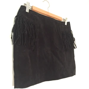  - Kjol i mocka, köpt i Spanien. Fransar på delar av framsidan samt hela baksidan. Bra skick.