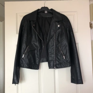  - Snygg jacka i skinnimitation. Svart färg med silver/metall-färgade dragkedjor. 