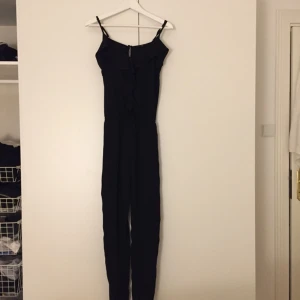  - Fin jumpsuit i svart från H&M, avsmalnande ben och smala axelband. Dekorativa volanger fram. Använd ett fåtal gånger, är i fint skick. Köparen står för frakten