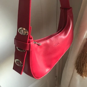 Trendig väska  - En fin bagett väska. Köpte den här på Plick så vet inte mkt bakgrunden vart den kommer ifrån. Röd med silver detaljer. Små skador på den men ingenting som gör att användningen störs😊 frakt till kommer! 