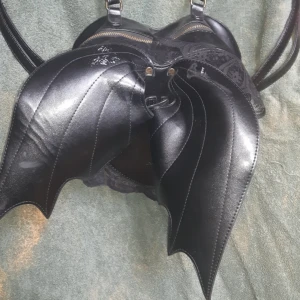  - Lite sliten men söt väska med axelband som kan ställas in i storlek.  Söta fladdermus vingar på ryggen. 🌙   Obs! Katt finns i hem 🙀   Kan hämtas upp i Malmö eller Hässleholm!