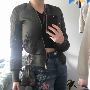  - Olivgrön bomberjacka med quiltade armar. Skönt ”glansigt” material. Färgen är något varmare i verkligheten. I nacken finns nån sorts fläck, men det syns knappt (sista bilden). Troligen på grund av hårolja. Pris kan diskuteras!  Sorry för smutsig spegel.