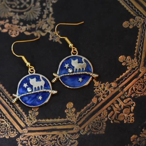 Örhängen med kattberlock - Handgjorda örhängen med guldpläterad berlock och nickelfria krokar 🌙 På min profil finns fler örhängen med berlocker i flera andra storlekar, färger och former! 🪐 Köp 1 par för 40kr, 2 par för 70kr, 3 par för 100kr! Örhängena levereras i en fin liten presentpåse. Frakt på 13kr tillkommer 💫