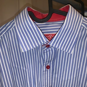 Randig skjorta med röda knappar - Skräddarsydd randig skjorta med röda knappar, i bra skick. Sitter som en stl L slim fit (man men passar kvinnor med). Sitter som en oversized skjorta om du har typ stl S-M. 