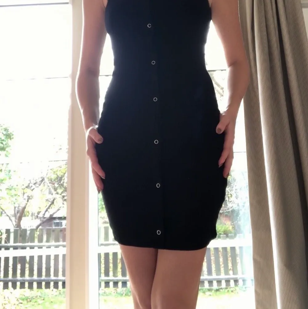 Liten svart klänning i Manchester liknade tyg. Stretchig med design knappar längs hela framsidan. . Klänningar.