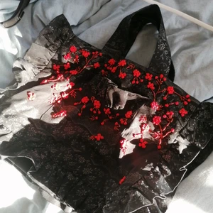 Svart blommig väska - Svart handväska med röda blommor och svagt silvrigt mönster, helt oanvänd lappar finns kvar. En väska som fångar ögat. Toppskick, inga hål eller några lösa pärlor. 