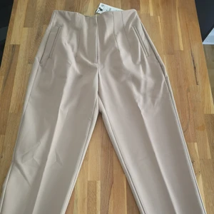 Byxa med hög midja Zara - Beige kostym/slacks från Zara. Hög midja, något kortare i benet. Markerade sömmar fram och bak, knäppning med dragkedja fram och metallhake. Oanvända. 