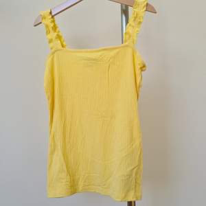 Ett gult linne med volang på axelbanden. Endast testade så i nyskick. Köparen står för frakten.