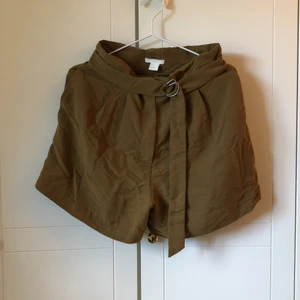 Shorts  - Superfina olivgröna shorts från H&M med fickor och reglerbart skärp i midjan! Endast använda en gång så jättefint skick! Säljer då de är för små. Köparen står för frakten.
