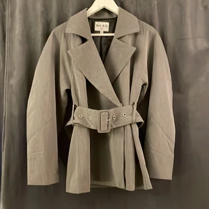 Grå Blazer från NA-KD  - Grå blazer med bälte och fickor från NA-KD. Stängs med 2 knapar och har stora ballongärmar. Storlek 34.