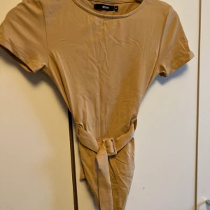 Beige body - En beige body med insytt bälte för extra detalj. Super fin och bekväm men kommer tyvärr ej till användning. Luftigt material.