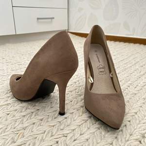 Pumps i mocka imitation i färgen beige/mörkbeige. Klackhöjd ca 9cm. Innesulan är i äkta läder för ökad komfort. Finns två defekter på skon, se bild. Förövrigt varsamt använda.