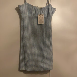 Klänning st M - Vit/blå rutig klänning från pull&bear i st M, på andra bilden är de samma klänning fast i anan färg men så man ser ungefär hur den ser ut på. Köpt förra våren men aldrig använd då jag tyckte den var lite kort på mig. Om många intresserade så blir de budgivning.