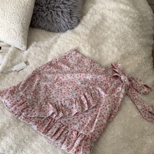 Blommig kjol - Säljer denna fina kjolen då jag av misstag klickade hem 2 st! Den är helt oanvänd💗Storlek S och den har även en dragkedja där bak, den är alltså inte så stretchig, man kan även knyta runt midjan med bandet på kjolen, superfint!💕 Buda privat