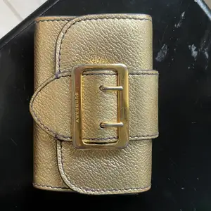Säljer äkta burberry plånbok i guld. Perfekt storlek att ha i väskan men ändå inte för liten så man tappar bort den. Unik design och färg. Den är väl använd så färgen har skavts av lite som man ser på bilden, annars bra skick. Har lådan kvar, minns inte exakt nypris men runt 4000.