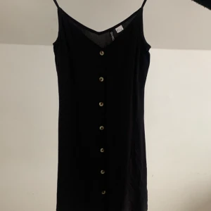 Svart klänning med knappar från H&M i storlek 34 - Hej jag säljer min svarta klänning från H&M i storlek 34 med beiga knappar. På mig som är 165 cm lång går klänningen ner till knäna. 