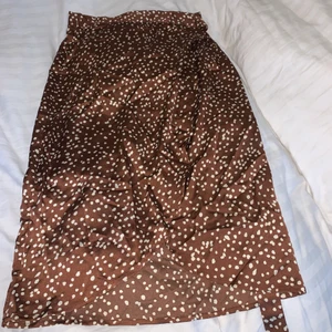 Kjol  - Brun prickig kjol i sidentyg, går omlott med knytning i midjan. Prislapp kvar. Storlek 40. 