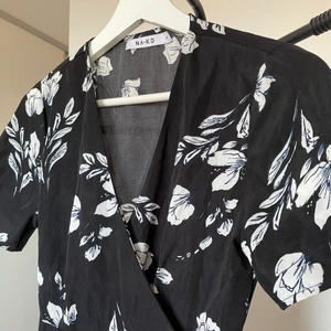 Omlottklänning - Superfin omlott klänning som slutar över knäna på mig. Säljer eftersom den blivit för liten för mig 😢 endast använd några gånger. Klänningen är svart med vita blommor och inslag av mörkblått. Väldigt skön och tunt tyg, perfekt till sommaren! Frakt tillkommer! 