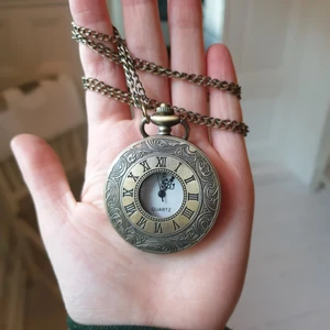 Klocka Halsband Kedja - Ett halsbandsur köpt i London. Ljus guldfärg med antik touch. Går att öppna med hjälp av en knapp ovanpå klockan men tiden visas även utanpå med hjälp av romerska siffror. Klockan har tyvärr slutat fungera men smycket är fortfarande lika snyggt! Ca 80 cm Ø. Kan mötas upp i Stockholm eller frakta:)