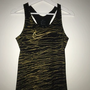 Nike träningslinne strl. XS - Ett svart linne med guldiga detaljer samt guldigt NIKE-märke på bröstet. Storlek XS. Stretchigt material. 