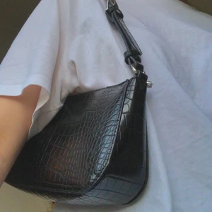 Svart baguetteväska med silverdetaljer  - Nästan oanvänd svart baguetteväska från Lindex, använd kanske en eller två gånger. I mycket gott skick. Inköpt i vintras men säljer pga att jag inte använder den. Nypris: 250 kronor. Endast leverans, köparen står för frakt!