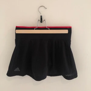 Tenniskjol i strl XS - Tenniskjol med inbyggda shorts. Snygg röd detalj i linningen. Köparen står för frakt. 