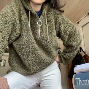 Grön teddy hoodie - En grön fluffig hoodie som är lite bredare, typ oversized (eller lite bredare i modellen) men även cropped (eller snarare lite kort, går fortfarande ner till midjan). Supermysig och trendig med cool runt ”spänne” på dragkedjan. Köptes second hand och säljs vidare då den inte kommer till användning längre. 