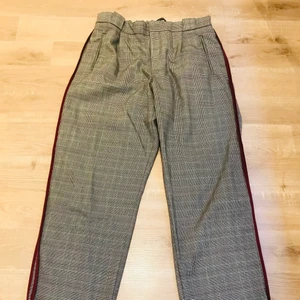 Kostymbyxor med röd rand - Fina kostymbyxor med resor där bak så väldigt bekväma. Två vinröda ränder längs benen. Skönt och luftigt tyg!