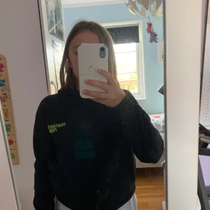 Svart Hoodie - Svart hoodie, med gul text på bröstet. Använd ett par gånger men i ett bra skick.