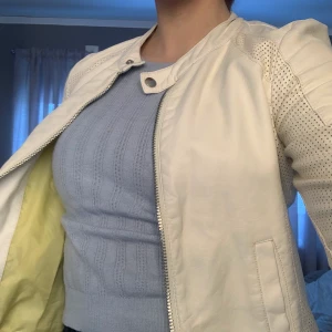 Vit skinnjacka med gul insida - Snygg skinnjacka från Noisy May med gult tyg på insidan. Säljer pga för liten i storlek. Inga skador, som ny. (Den har legat i en låda därav lite skrynklig på bilder , men det försvinner när den fått hänga på galge ett tag)