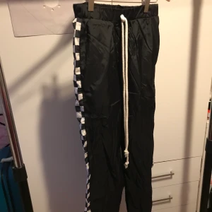 Svarta byxor - Svarta byxor med racing detalj vid sidorna. Kan vara bra att åka pulka med över byxor. Aldrig använd.