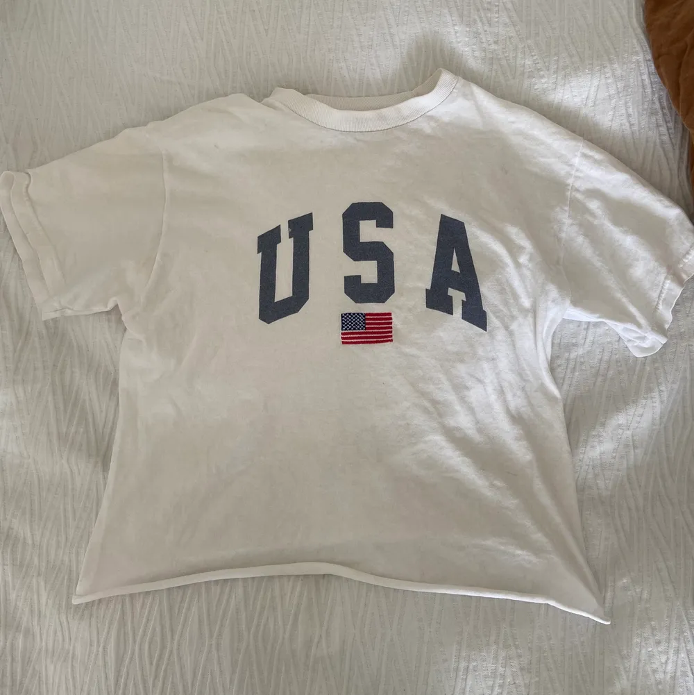 En slapp, vit T-shirt med USA-tryck i lite tjockare material från Brandy Melville. Passar XS-M. Originalpris: 300 kr.. T-shirts.