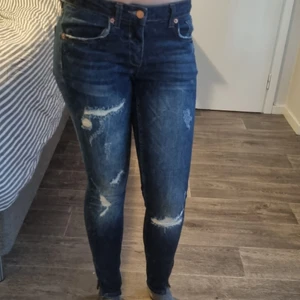 Slitna jeans med snygga detaljer 28/32 - Snygga "slitna" jeans med snygga detaljer i "roséguld" (knappar och dragkedja vid benslut) storlek 28/32. Låg till normal midja, ej hög.  Från Gina tricot. Sparsamt använda. 