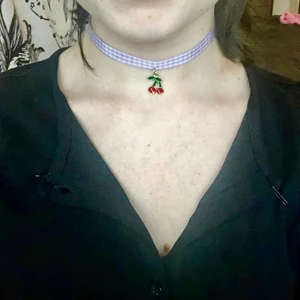 Lila choker med körsbär - Lila rutig tygchoker med ett litet körsbärs smycke på. Superfint och i nyskick men kommer tyvärr inte till använding♥️
