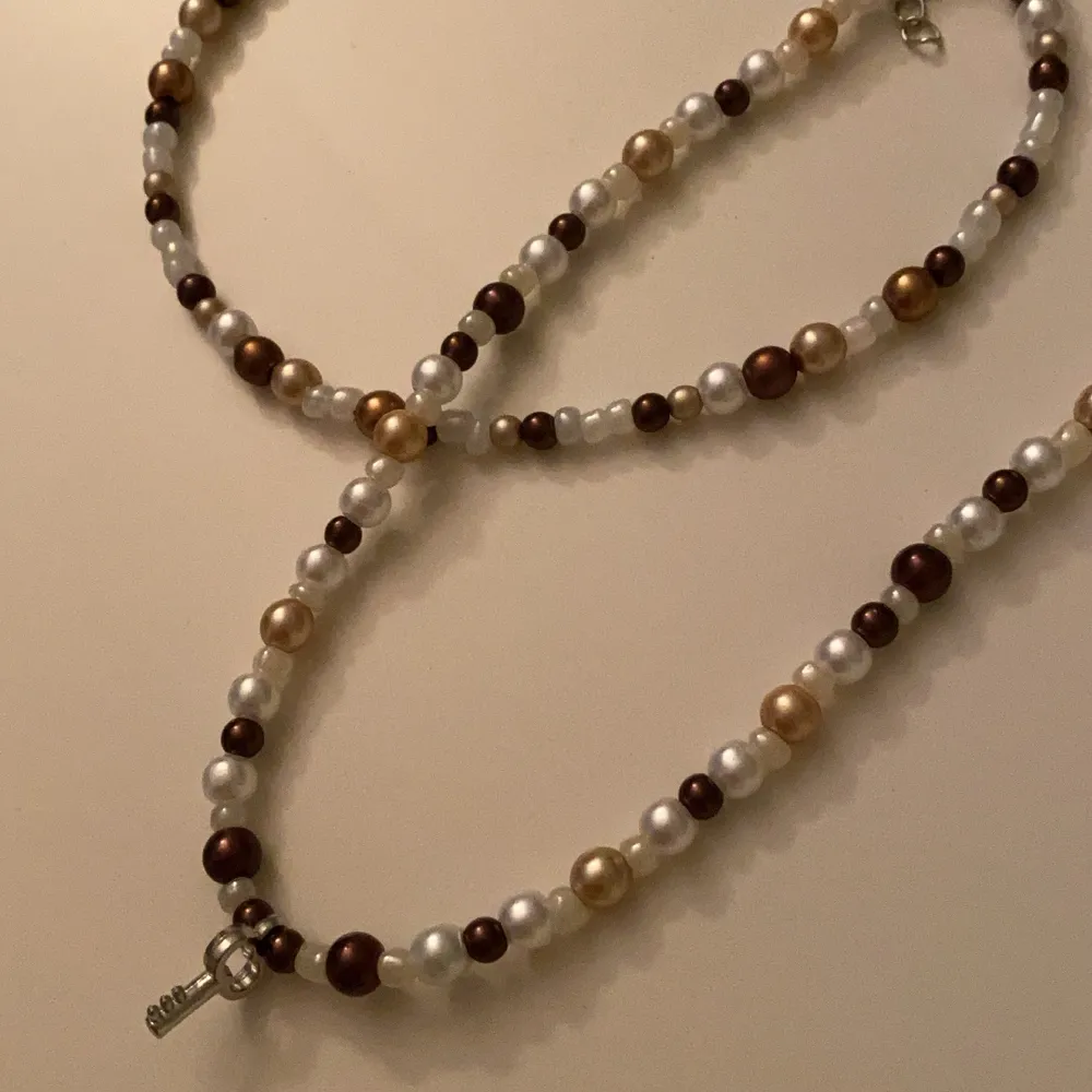 Två stycken handgjorda halsband med bruna pärlor, ett halsband med en nyckel och ett med bara pärlor. Lite större än en choker . Accessoarer.