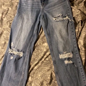 Blåa jeans från NA-KD - Ett par blåa jeans med hål på knäna, även ett hål på vänstra låret. Dom är även upp till. Säljer för att dom inte passar längre, dom är i riktigt jeans material, alltså inte stretchiga💞 Nypris 400 och dom är använda någon enstaka gång. Frakten står du själv för💞