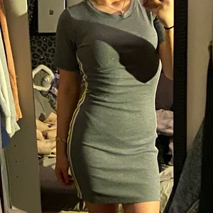 Grå tajt klänning med färgglada sträck  - En tajt hyfsat lång klänning med neon gult och ett vitt sträck på varsin sida. Klänningen har tyvärr inte används men tycker den är as snygg 