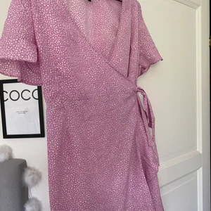 Rosa klänning från VeroModa - Rosa tunn klänning med vita prickar perfekt till sommaren! Tvättad 1 gång. Omlott klänning - du knyter den när du tar på dig den.