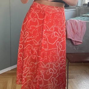 Skjol med mönster - En kjol köpt från en butik på Turkiets flygplats. Väldigt fin och väldigt bekväm. Endast använt 2 gånger under semestern, växte ur den snabbt. Det är ett mesh material på utsidan med snyggt mönster, undertill finns det en underkjol. Midjebandet är inte justerbart, på sidan sitter en dragkedja. Den är en orange/röd färg, med vitt mönster.