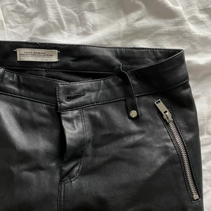 Läder/skinn liknade byxor från Zara - Ett par riktigt coola byxor från Zara som tyvärr har blivit för små för mig. De är i läder liknade material med detaljer på knäna & silverdragkedjor på olika ställe. Även dragkedja i slutet av varje ben så det blir som en slits. Fint skick men en söm har låsnat där man kan trä ett bälte (se första bilden), men inget man tänker på. Fler bilder kan skickas. Stl S men passar nog även XS. Köparen står för frakten, priset kan diskuteras. 💕💕