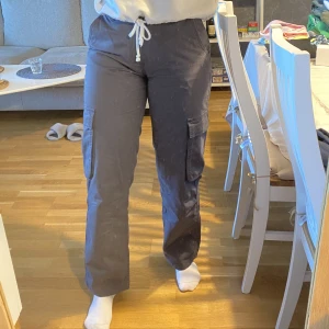 Grå cargobyxor  - Grå lågmidjade cargobyxor från Gina i Stl 38 Använda endast 2 gånger men märkte att de redan måste ha varit trasiga när vi köpte dem.  Hål vid ena öglan och bak på låret, men båda är ihopsydda så gott de går❤️‍🩹  Nypris 399 Fler bilder kan skickas