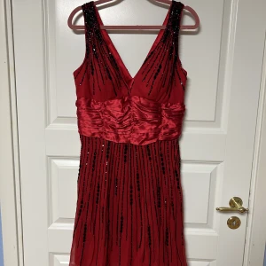 Röd klänning med svarta detaljer  - Festklänning, aldrig använd, storlek 38-40. Enstaka pärlor saknas vid nära titt, men extra pärlor/paljetter finns.