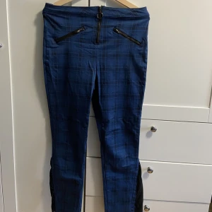Alternativa långbyxor - Skitsnygga alternativa blå-rutiga highwaisted långbyxor med dekorations dragkedjor och snygg metalldetalj i gylfen, storlek L, köpt på Hot Topic, självgjort ”flare” längst ner på byxbenen, i väldigt fint skick, i princip oanvända
