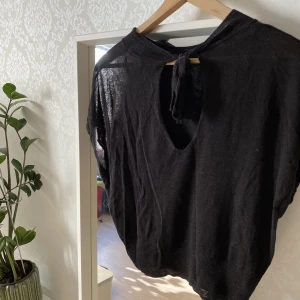 Svart tröja med knytning på ryggen - Svart tröja som man knyter på ryggen. Slapp och ledig i materialet men ger en fin form.