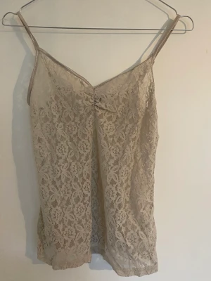 Spetslinne med satinband - Gulligt linne i spets med justerbara band i en fin beige/rosa färg. Tecken på användning men är i fint skick.